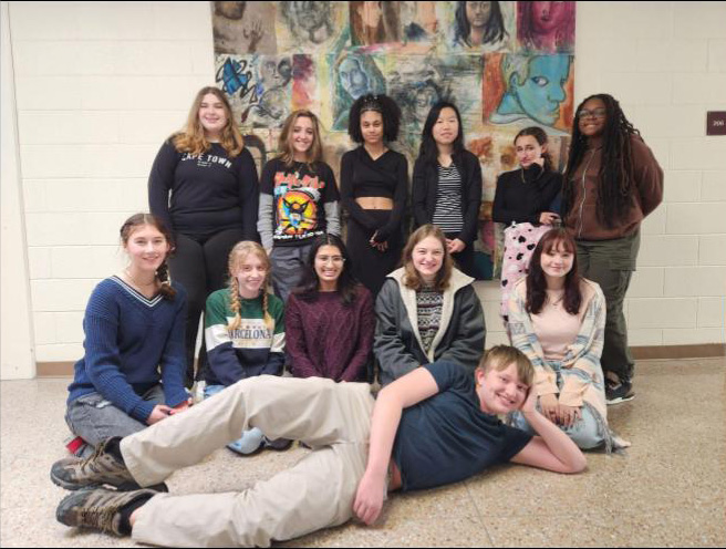 A group of 12 high school kids - six standing in back, five squating in front and one lying across the front of all - smile.