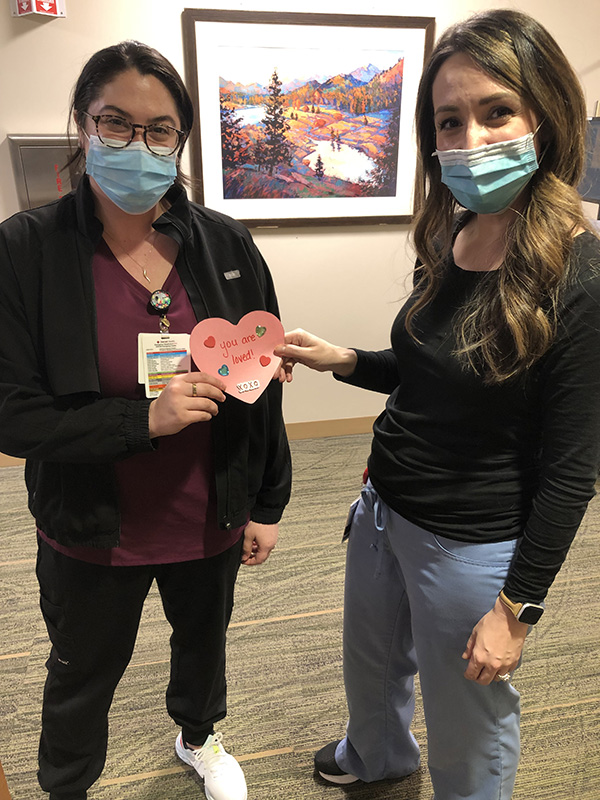 Two women in nurse scrubs hold a pink hear-shaped Valentine.