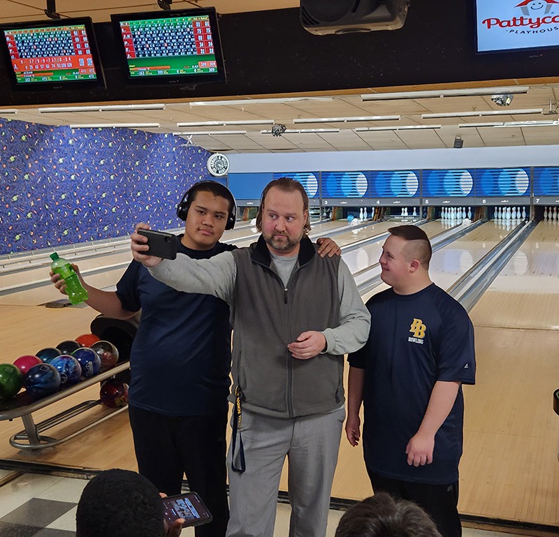 A man in center and two young men on his sides stand together taking a photo. 