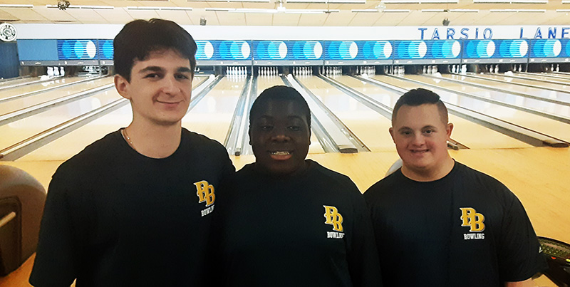 A group of three young men, all wearing navy blue shirts with PB on the right side. They are smiling.