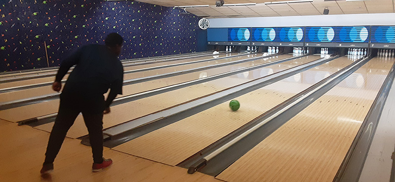 A young man wearing dark clothes just released a bowling ball down the alley.