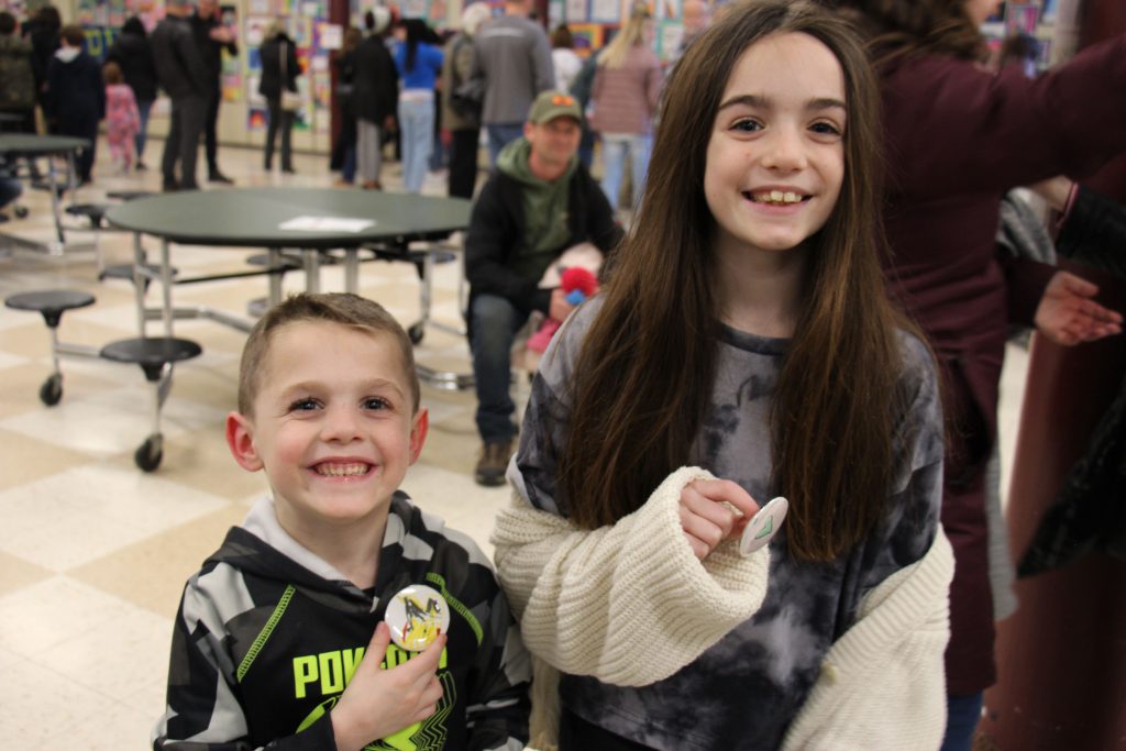 Two elementary students - a little boy on the left and an older girl on the right - hold the buttons they made.