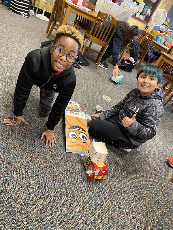 Two fourth-grade students smile as they work on their recycled cars.