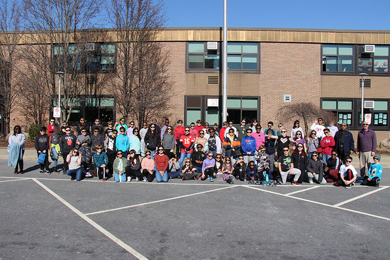 A group of about 80 fifth-grade students standing outside in front of a big brick building on a beautiful day with a bright blue sky.