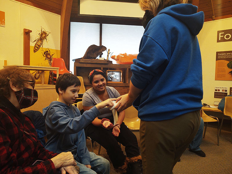 A woman in a blue hoodie holds out an animal as a middle school boy pets it.