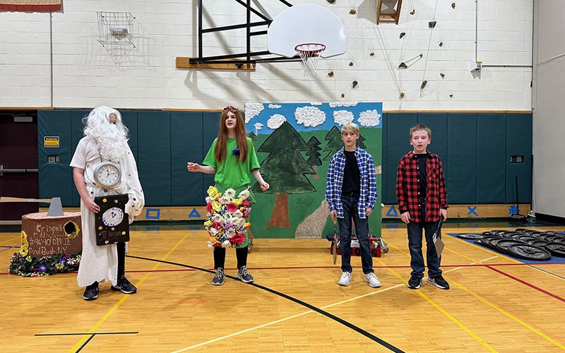 A group of four middle school students in costumes stand in a gym.