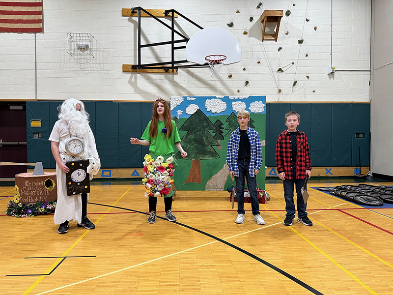 A group of four middle school students in costumes stand in a gym.