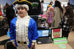 A third-grade boy dressed in a white wig, three-point hat and a colonial uniform. He is Alexander Hamilton.