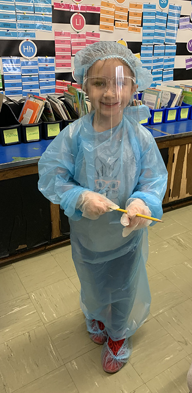 A second grade girl is dressed in light blue scrubs and a blue hair covering as she talks about being a dentist.