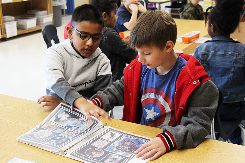 Two second grade boys look through a binder of artwork.