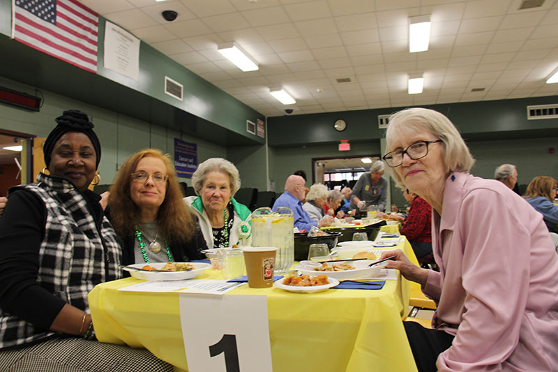 A table with a yellow table cloth and the number one hanging on it. There are four women sitting at it and smiling.