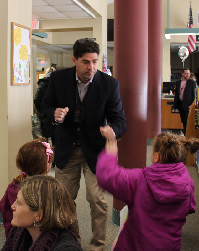 A man in a blue jacket and button-down shirt gives a fist bump to a little girl with pig tails wearing a pink jacket.