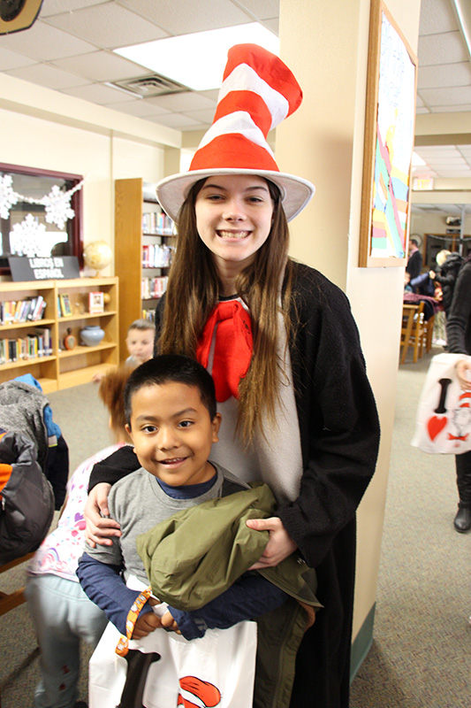 A high school girl dressed in a cat in the hat costume stands with a kindergarten boy with dark hair. Both are smiling broadly!