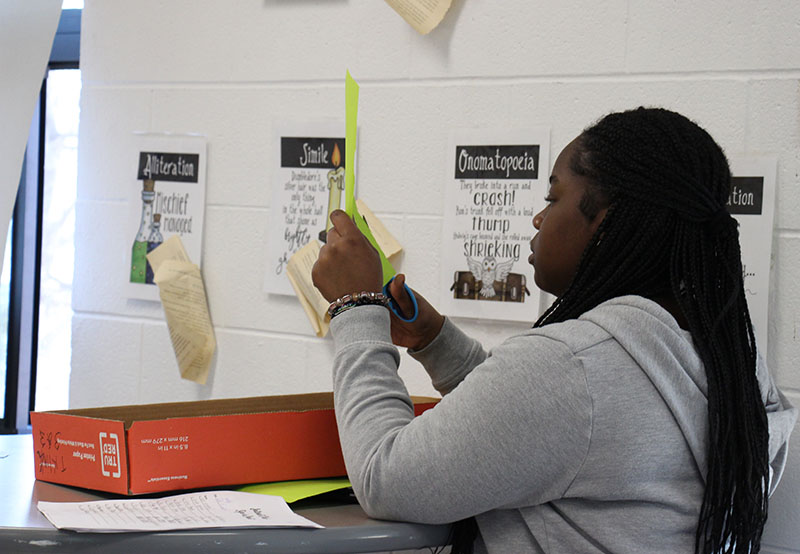 A middle school student cuts out a sign from a piece of construction paper.
