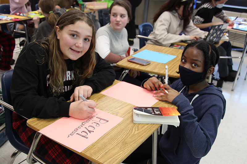 Two middle school girls at a desk creating signs for recycle bins.