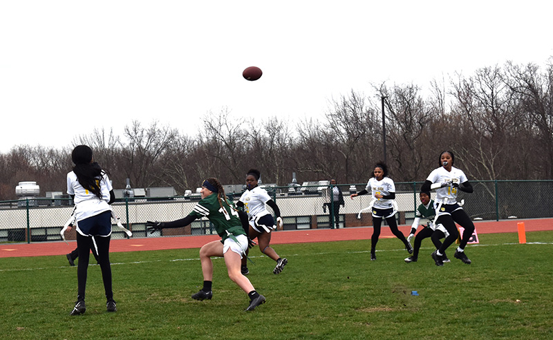 A football sails through the sky as players in white shirts go toward it. A player in green goes after it too.
