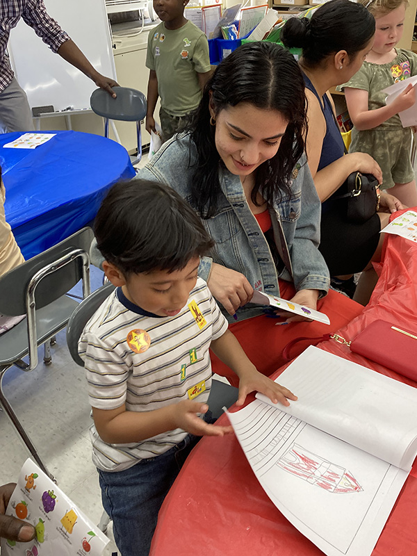 A kindergarten boy reads his book he created to a woman sitting next to him.