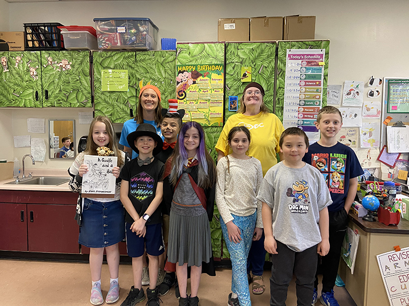 Seven students and two women stand together smiling. They have  costumes on.