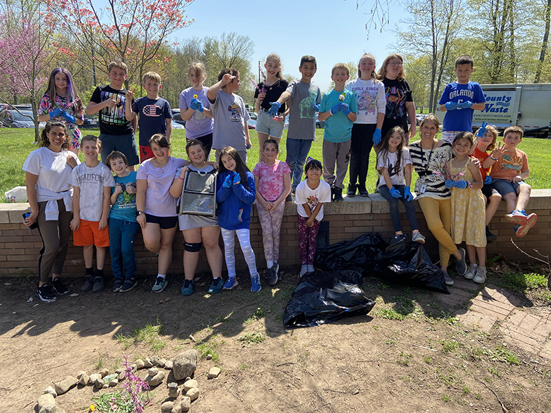 Two rows of fourth-grade students stand in a garden they just helped to weed.