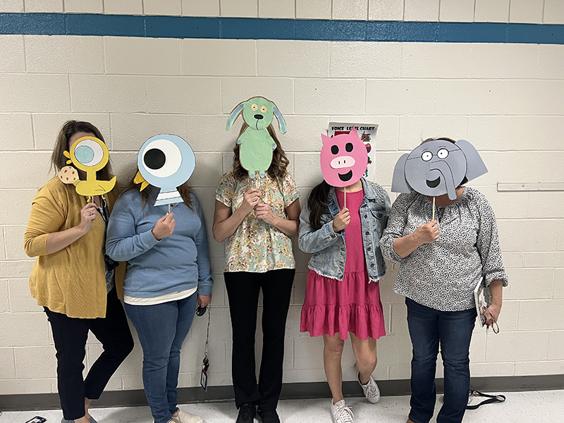 Five women stand holding pictures on sticks of animals in front of their faces.