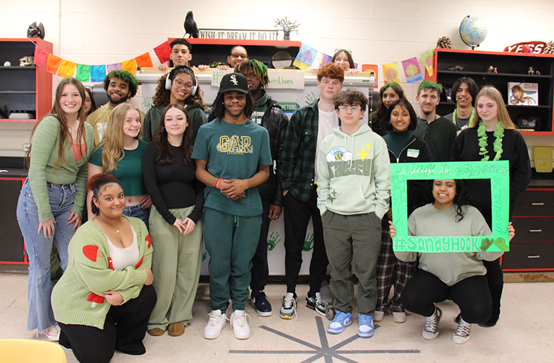 A group of 18 high school students stand together, all wearing green.