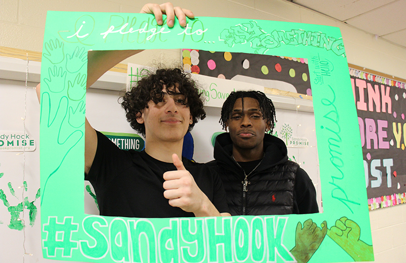 Two high school kids, both boys, give thumbs up as they hold up a green frame that says Say something.