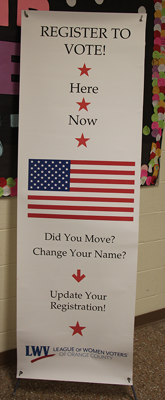 A large vertical sign with an American flag on it says Register to vote here.