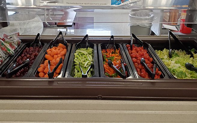 A salad bar with lettuce, carrots, tomatoes, cucumbers and many other choices.