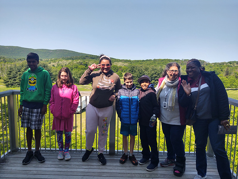 Six middle school students stand and smile with a mountain in the background. There is an adult on the right smiling too.