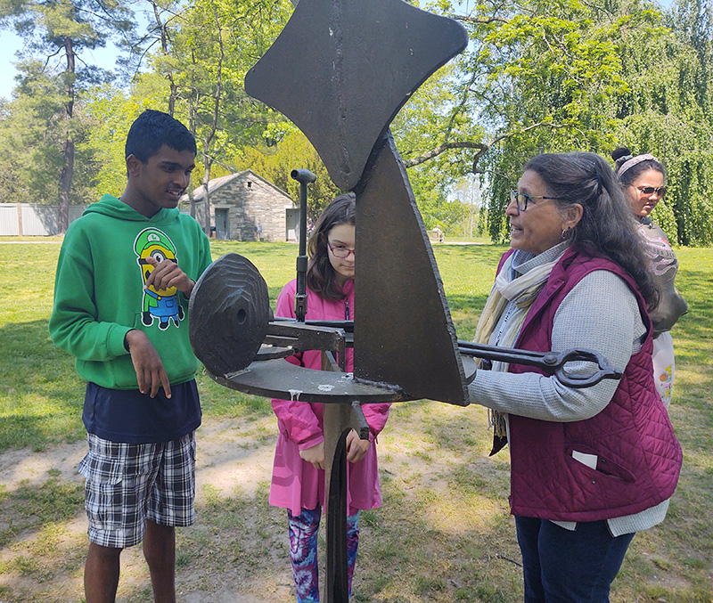 Two middle school students look at an interesting piece of metal sculpture with an adult.
