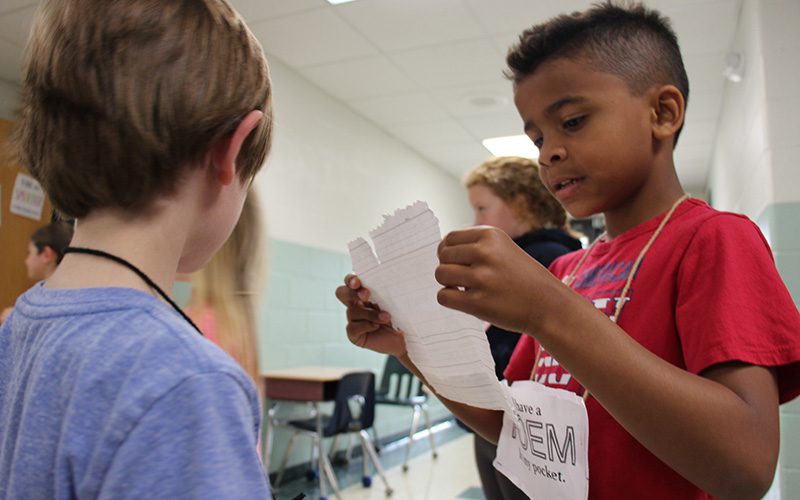 Two boys stand together while the boy on the right reads his poem to the boy on the left.