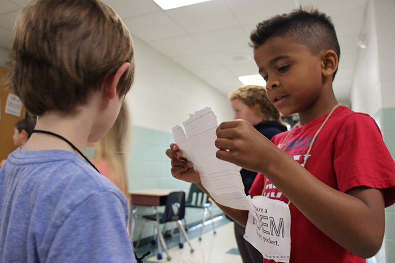 Two boys stand together while the boy on the right reads his poem to the boy on the left.