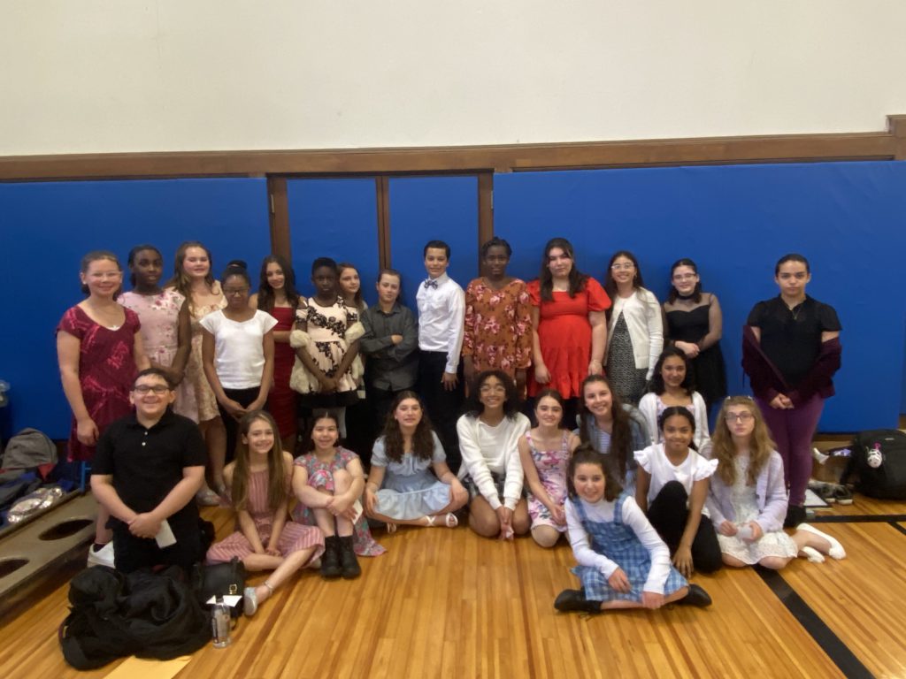 A group of more than 20 elementary and middle school students sitting and standing in a gym.