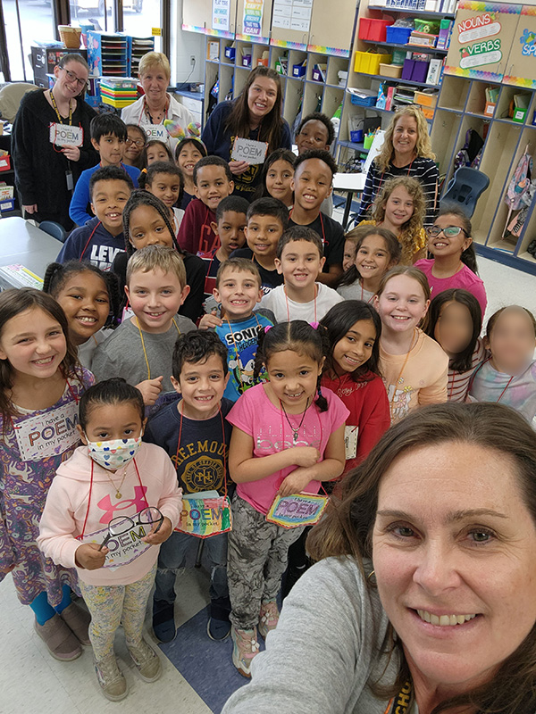 A selfie photo of two second-grade classes all standing together with their Poem In Your Pocket around their necks. There are three adults in the photo too.