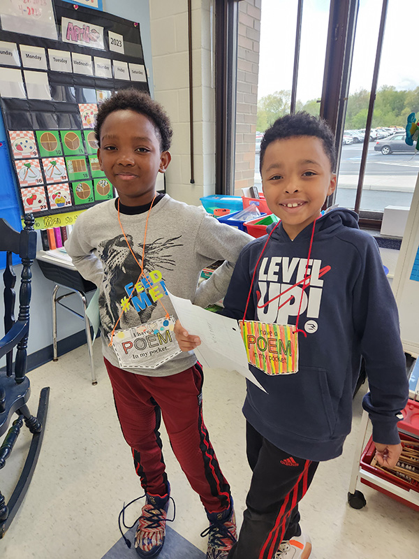 Two boys smile with their poem in Your pocket hanging from their neck.