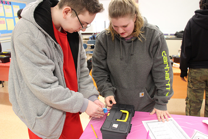 Two high school students attempt to unlock a black box that sits on a table.