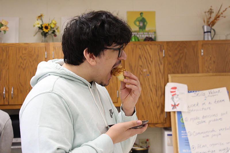 A high school student wearing a gray hoodie eats a baked good.