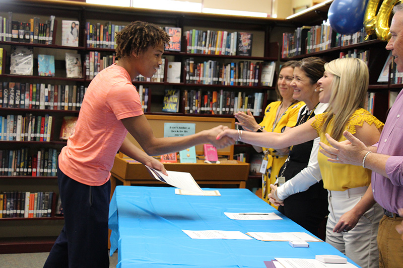 A high school boy in a peach colored tshirt shakes hands with a woman and accepts an award from her.