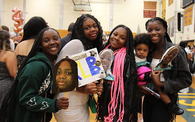 A teacher serves during the volleyball game with students watching in background
