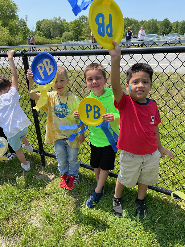 A group of elementary kids hold painted plates up that say PB in blue and gold.