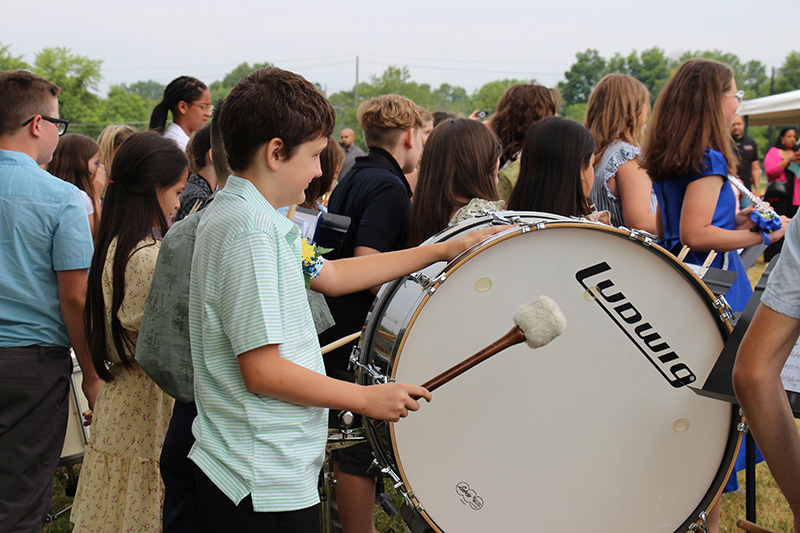 A fifth-grade boy drums a large drum.