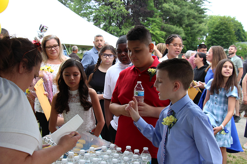 A group of fifth-grade students stand at a table getting water and cupcakes.