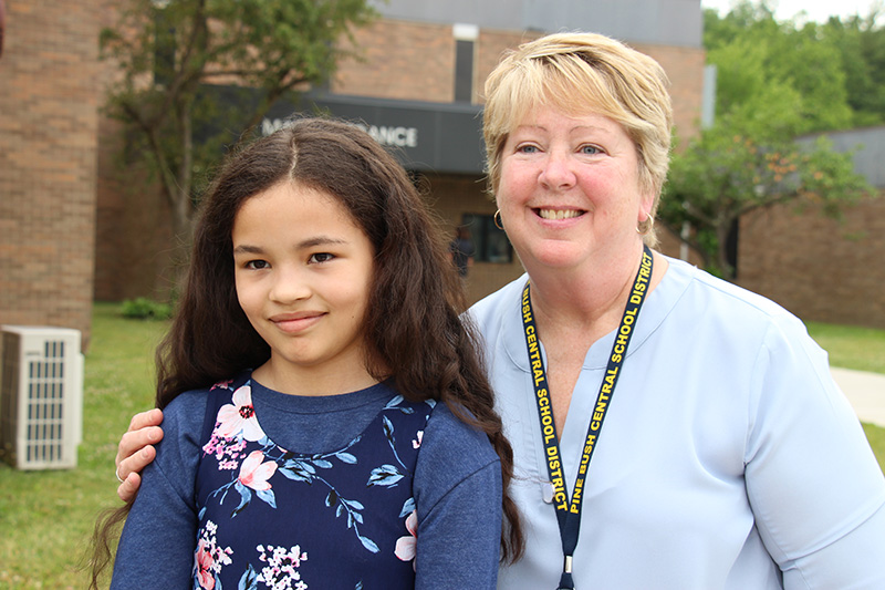 A woman with short blonde hair smiles with her arm around a  fifth-grade girl, with long dark hair. 