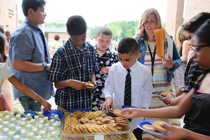 A group of fifth-grade boys all dressed nicely stand around a table getting cookies.