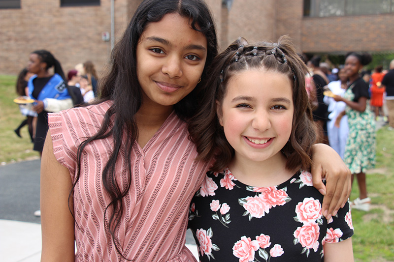 Two fifth grade girls, both with dark hair, stand together smiling.