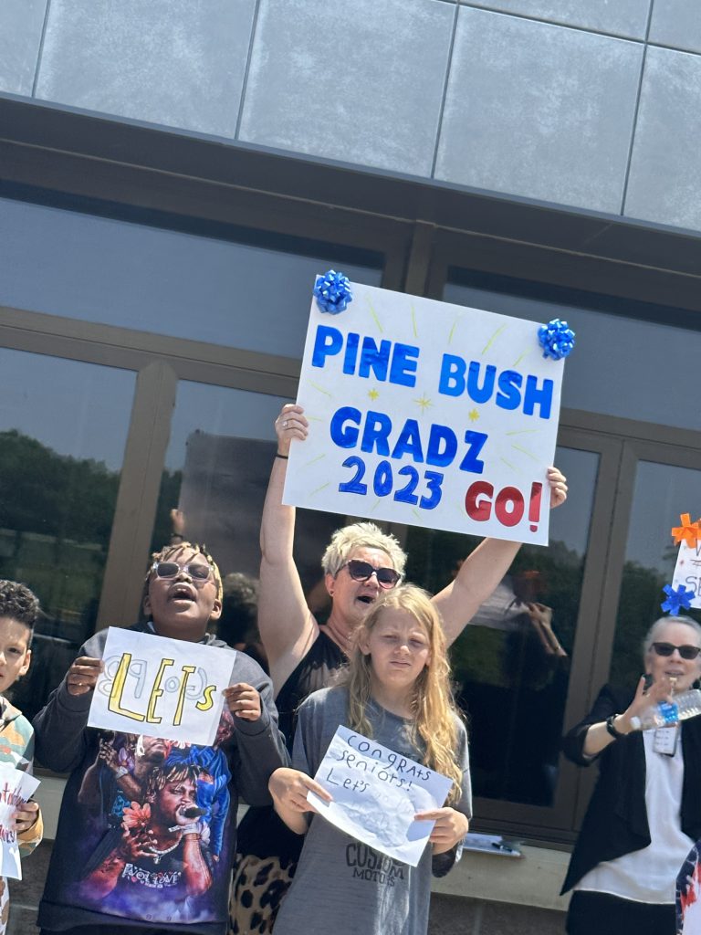 A group of adults  standing holding signs in support of graduates. One says Pine Bush Gradz 2023 Go!