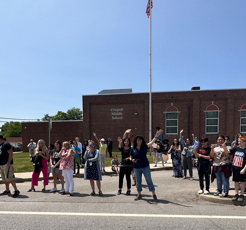 A group of staff and middle school students wave as the bus passes by.