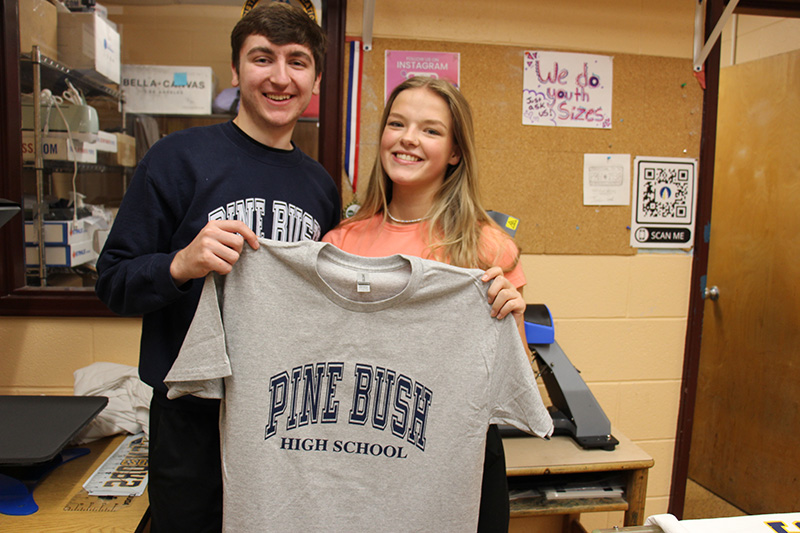Two high school students hold up a shirt that says Pine Bush.