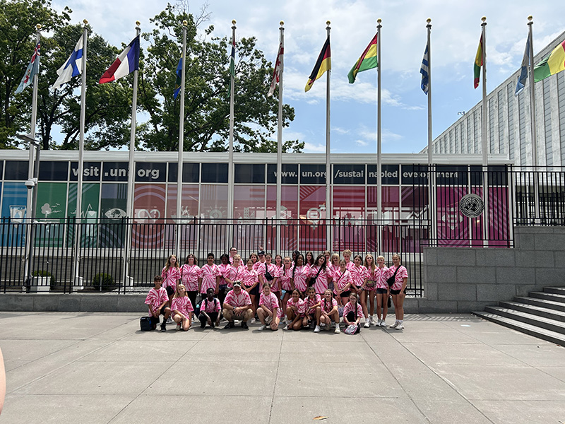 A group of 33 middle school students, all wearing pink tie dye t shirts, in front of the United Nations building.