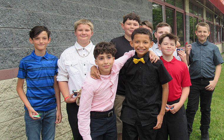 A group of eight fifth-grade boys stand together smiling.
